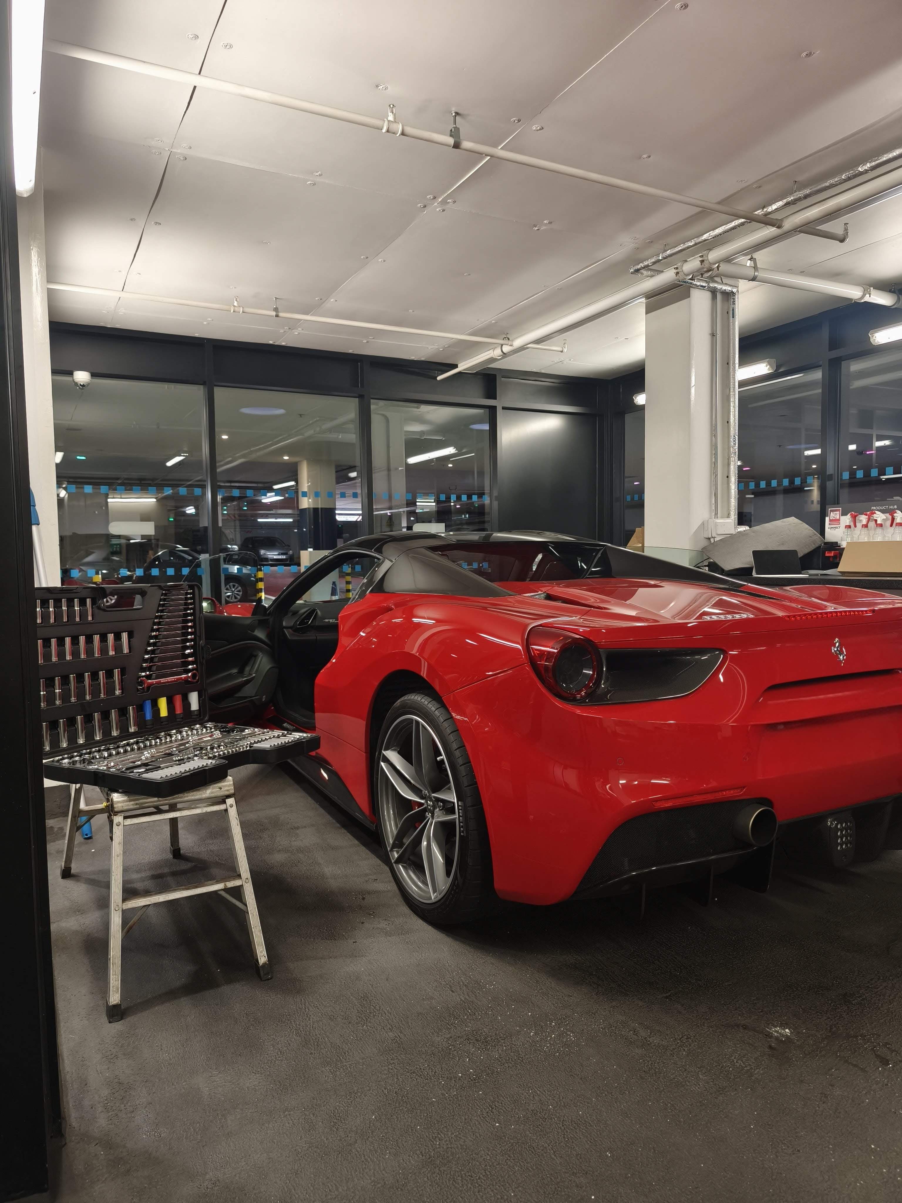 Red sports car in a showroom with tools and equipment on a stool.