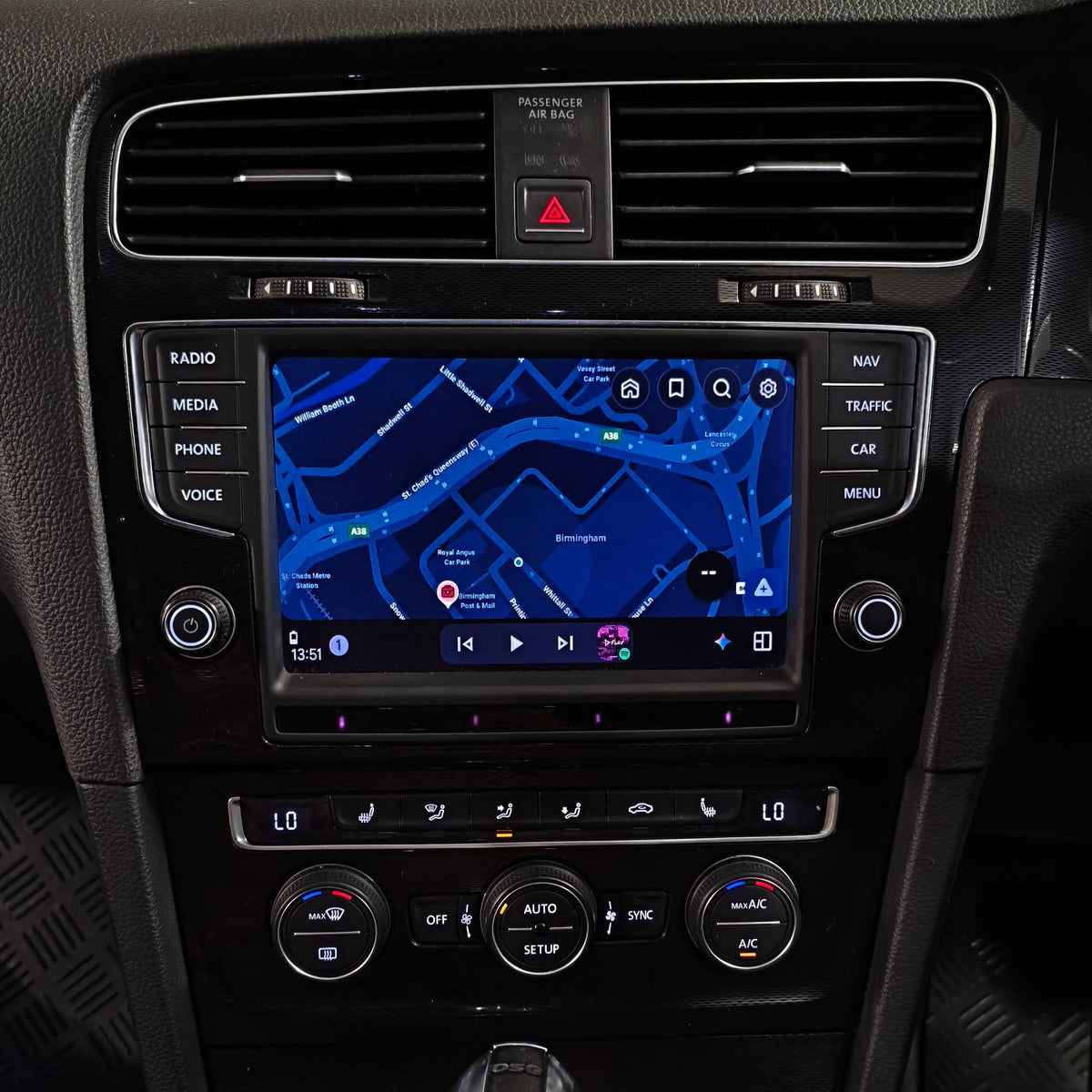 A car's center console featuring a large touchscreen infotainment system with a blue navigation map, climate control dials, and a gear shifter.